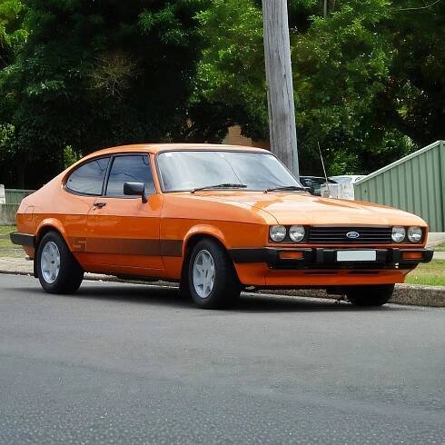 An orange, 1983 Ford Capri S coupe, parked on a road.
