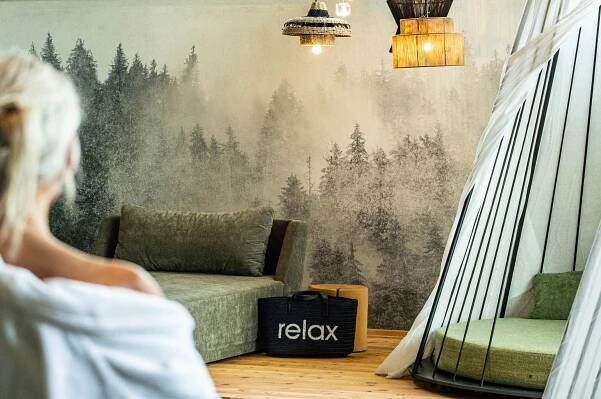 Zimmer mit Waldtapete, Sofa, Lampe und Tasche mit Aufschrift "relax"