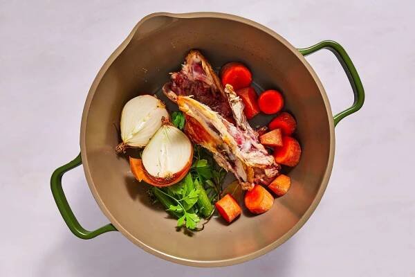 A large pot with chicken carcass, onion, carrot, celery, garlic, tarragon, parsley, and bay leaf