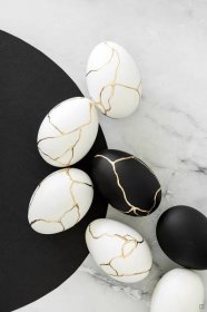 black and white eggs with cracked ones on a marble table top next to an egg holder