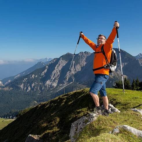 Ein Wanderer steht mit ausgestreckten Armen vor einer beeindruckenden Berglandschaft.