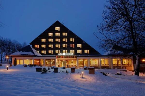 a large building with lights in the snow at night at Hotel Krakonoš in Mariánské Lázně