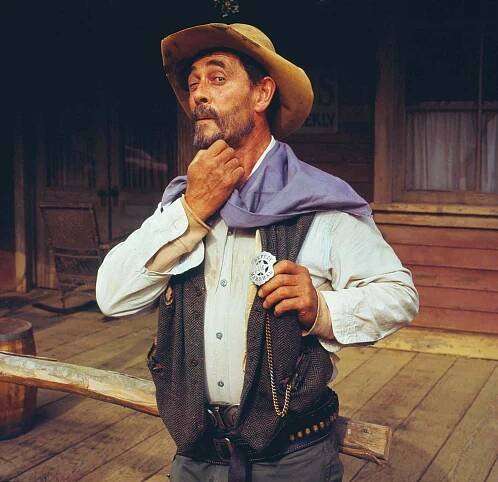 Ken Curtis dressed in a cowboy outfit, standing with a thoughtful expression