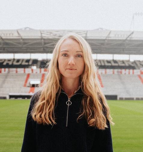 Die junge Nachhaltigkeitsmanagerin des FC St. Pauli steht im Millerntorstadion und blickt ernst in die Kamera.