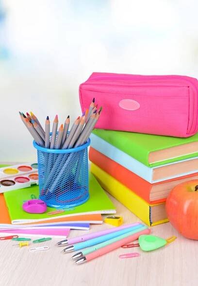 several books, pencils and an apple on a table with other school supplies in the background