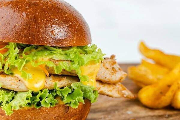 Free Close-up of a juicy chicken burger with cheese, lettuce, and fries on the side, perfect for food photography. Stock Photo