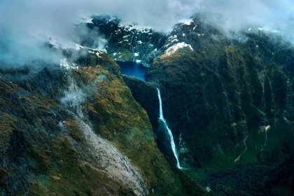 A mountain lake feeds into a waterfall on a scenic flight from Queenstown to Milford Sound.