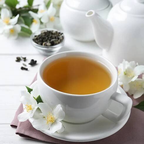 Cup of tea and fresh jasmine flowers on white wooden table. Space for text