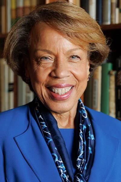 Head and shoulders portrait of Angela Kinney, smiling, wearing a blue suit jacket and dark blue scarf
