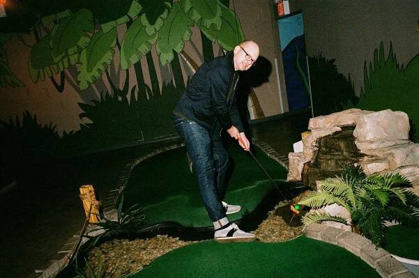 A man in a blue jacket and jeans plays mini-golf