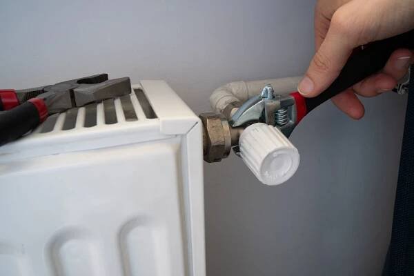 hands use pliers to tighten water leaks near radiator on wall