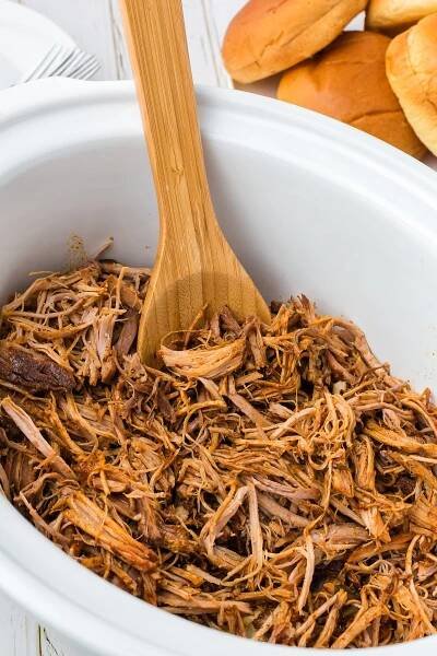 Slow Cooker pulled pork in a white crockpot after being shredded with a wooden spoon in the crockpot