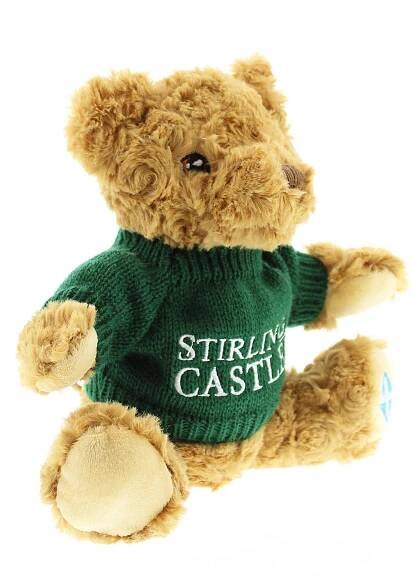 Small cuddly teddy bear wearing a green jumper with white text that reads Stirling Castle. The bear has a St Andrew's flag on it's left paw.  - Image