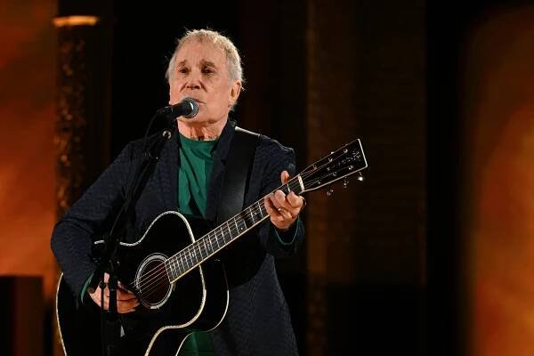 Paul Simon playing an acoustic guitar during a concert.