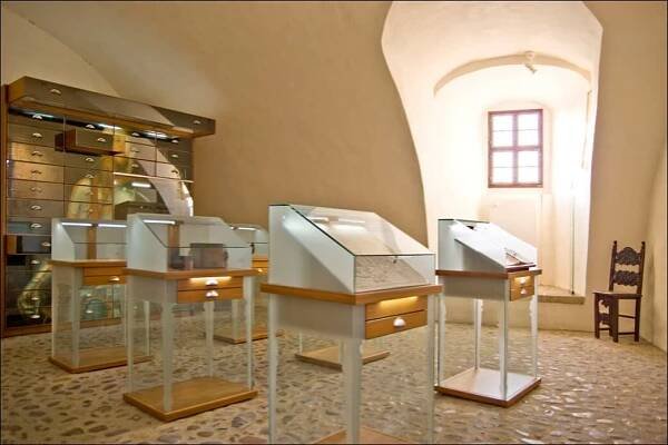 Blick in den unregelmäßigen Raum zur Amtsgeschichte. Er ist mit Wildpflaster ausgelegt. in der Raummitte stehen sechs halbhohe, vorn angeschrägte Ausstellungsvitrinen. In der rechten Ecke steht ein gedrechselter Stuhl, in der rechten Ecke ein Schrank.