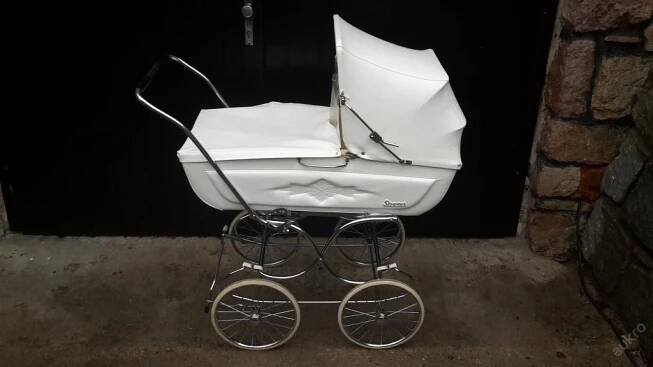 a white baby carriage sitting in front of a black door with the handlebars down