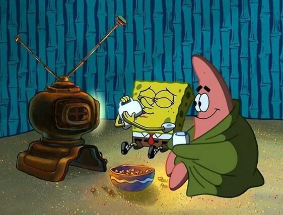 SpongeBob and Patrick sit on the floor, watching TV and eating popcorn under a green blanket. They look cozy and happy in a cartoon setting