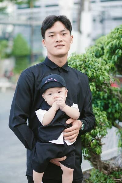 Free A father in black attire holds his baby son outdoors, capturing a touching moment. Stock Photo