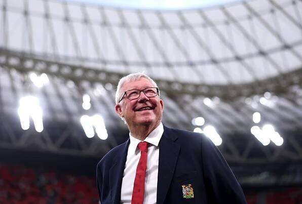 Sir Alex Ferguson smiling at a stadium.