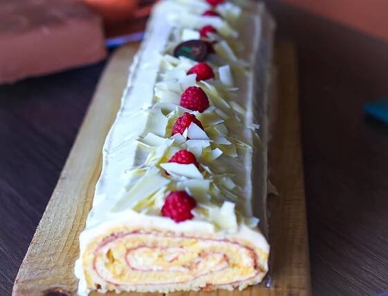 a long cake with white frosting and raspberries on top