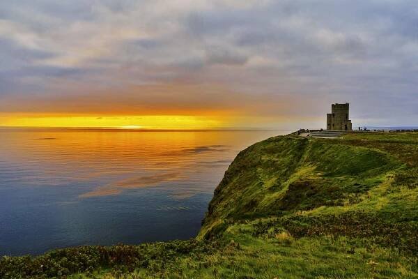 Der O'Brien's Tower, der sich am Rande der Cliffs of Moher erhebt, während ein leuchtend orangefarbener Sonnenuntergang über dem Atlantik zu sehen ist.