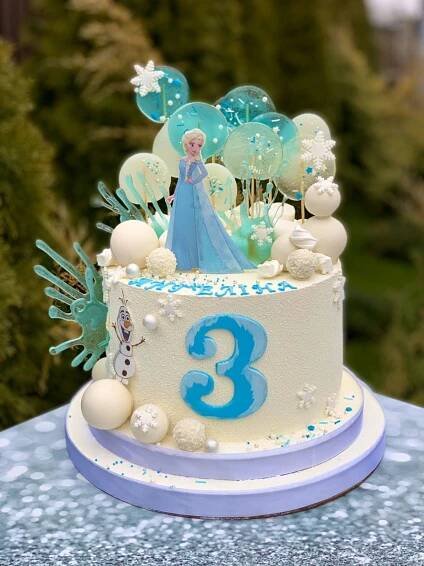 a frozen princess themed birthday cake with balloons and stars on it's top, sitting on a blue table cloth