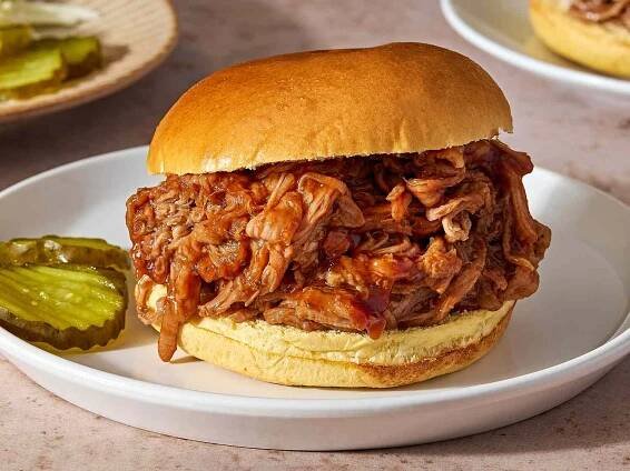 Slow Cooker Pulled Pork on a bun with pickle slices on the side