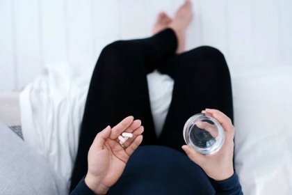 Woman taking medication with a glass of water in hand.