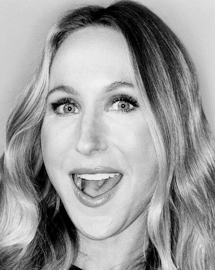 In a black-and-white close-up, a woman with an open-mouth smile looks brightly at the camera.