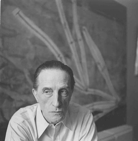 Portrait of artist Marcel Duchamp, 1952, posing in front of his 1914 painting "Network of Stoppages."