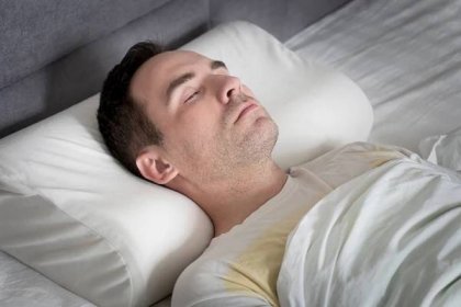 Roztomilý mladý muž spí na posteli na ortopedickém polštáři — Stock obrázek