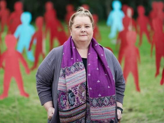A woman wearing a purple patterned scarf stands in a park in front of cardboard cut out people.