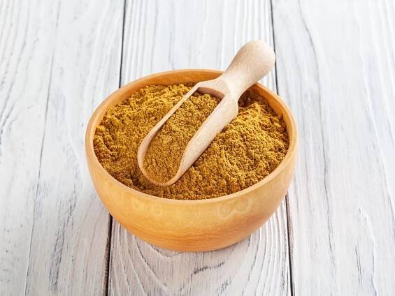 A bowl of curry powder with a measuring spoon on top. 