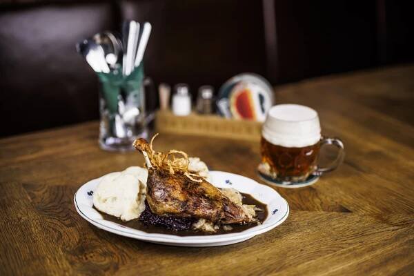a white plate topped with meat and mashed potatoes next to a glass of beer