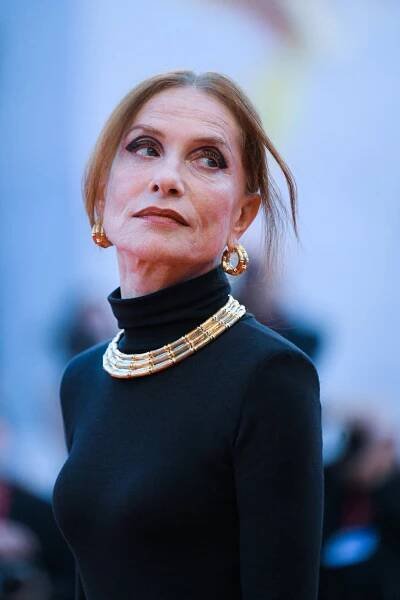 Isabelle Huppert wearing a black dress with gold earrings and a gold necklace.