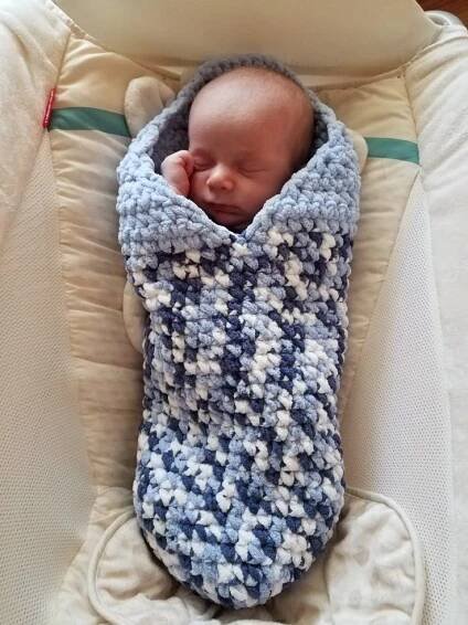 a baby sleeping in a crocheted blue and white blanket wrapped around it's head