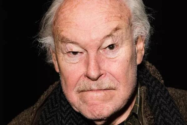 Timothy West in a striped shirt and brown jacket.