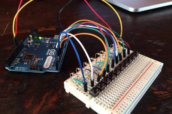 An Arduino Leonardo connected to a breadboard. On the breadboard are 10 buttons, each has a resistor and a wire connected to the arduino. A laptop is in the background.. Picture taken by Steven LeMieux