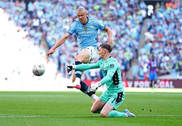 Erling Haaland of Manchester City shoots at goal, with Crystal Palace's goalkeeper diving to make a save.