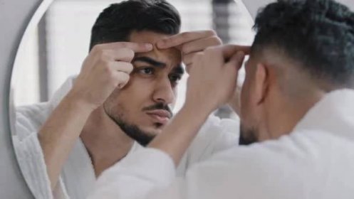 Nešťastný arabský arabský vousatý muž, který se dívá do zrcadla v koupelně a bojí se o problémy s kůží na obličeji. Úzkostlivý tisíciletý chlap mačkající pupínek dotýkající se obličeje frustrované černé hlavy péče o pleť — Stock záběr