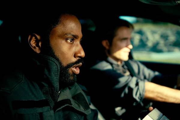 John David Washington and Robert Pattinson stare straight ahead in a vehicle.