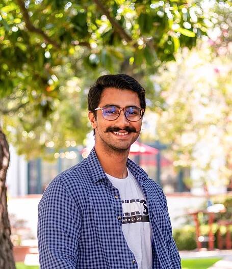 Ahmad wears a blue shirt and sits on a wall outside.