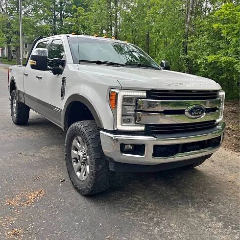 White Ford pickup truck parked on a road with trees in the background.