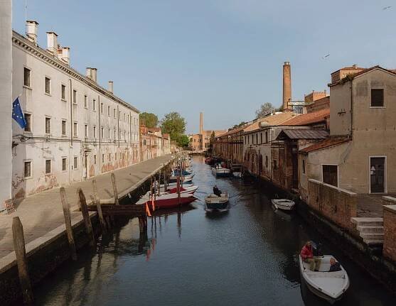 On a sunny day, looking straight down a canal that is filled with boats and has centuries-old cream-colored and tan buildings on both sides of the water.