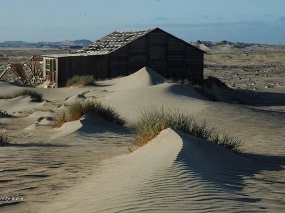 A sand dune merges with an old ruined house.