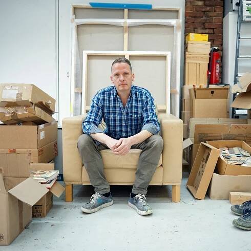 Der Maler Norbert Bisky sitzt auf einem Sofa in seinem Atelier. Norbert Bisky ist einer der wichtigsten zeitgenössischen deutschen Künstler, seine Werke sind in den bedeutendsten Museen der Welt zu sehen etwa dem MOMA in New York. Er verbindet Gemälde- und Bühnenkunst. (Foto: picture-alliance / Reportdienste, picture alliance/dpa | Carsten Koall)