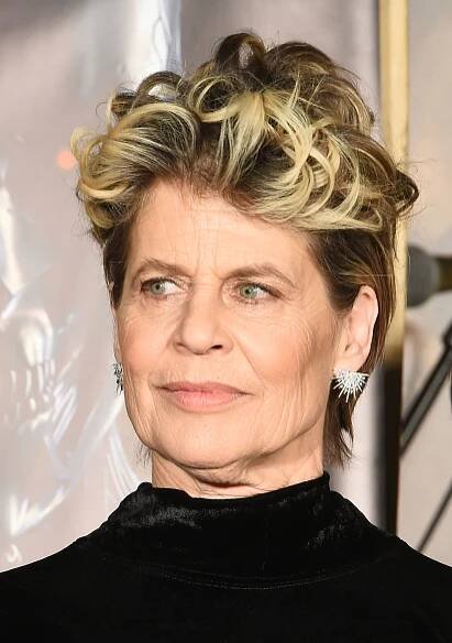 Linda Hamilton with styled short hair and star-shaped earrings wearing a high-collared velvet top, looking slightly to the side