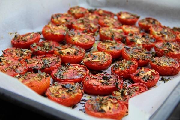 a tray filled with lots of sliced tomatoes on top of a stove burner and topped with seasoning