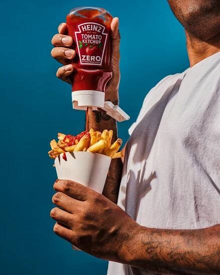 Person pouring Heinz Tomato Ketchup Zero onto french fries.