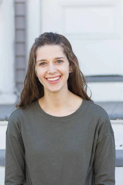 Headshot of woman smiling with long brown wavy hair wearing a dark green sweater